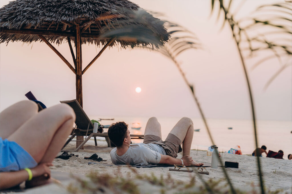 Travellers relaxing on a Zanzibar beach under a thatched umbrella at sunset